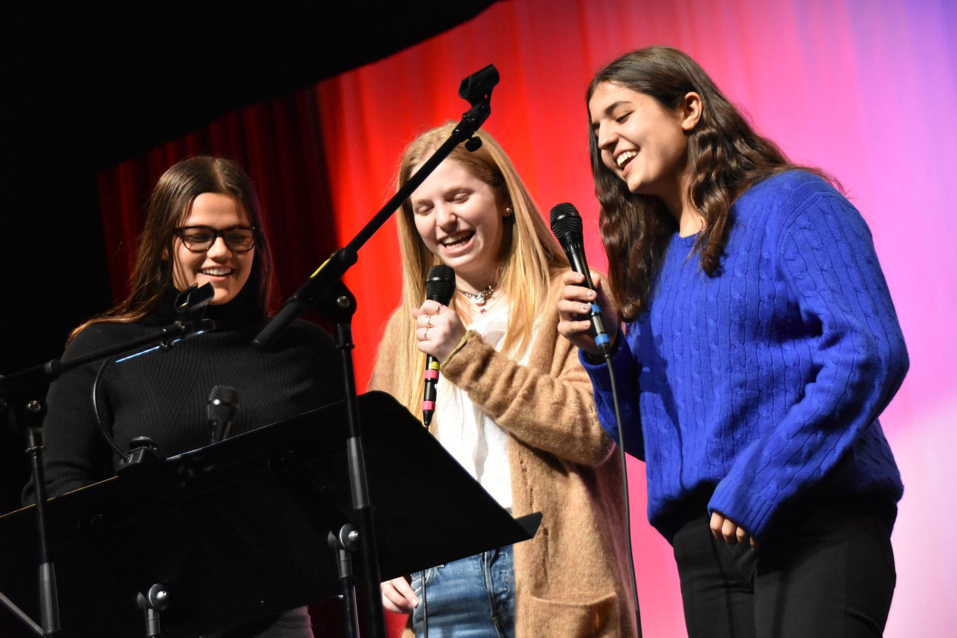 Three people smiling and singing into microphones.