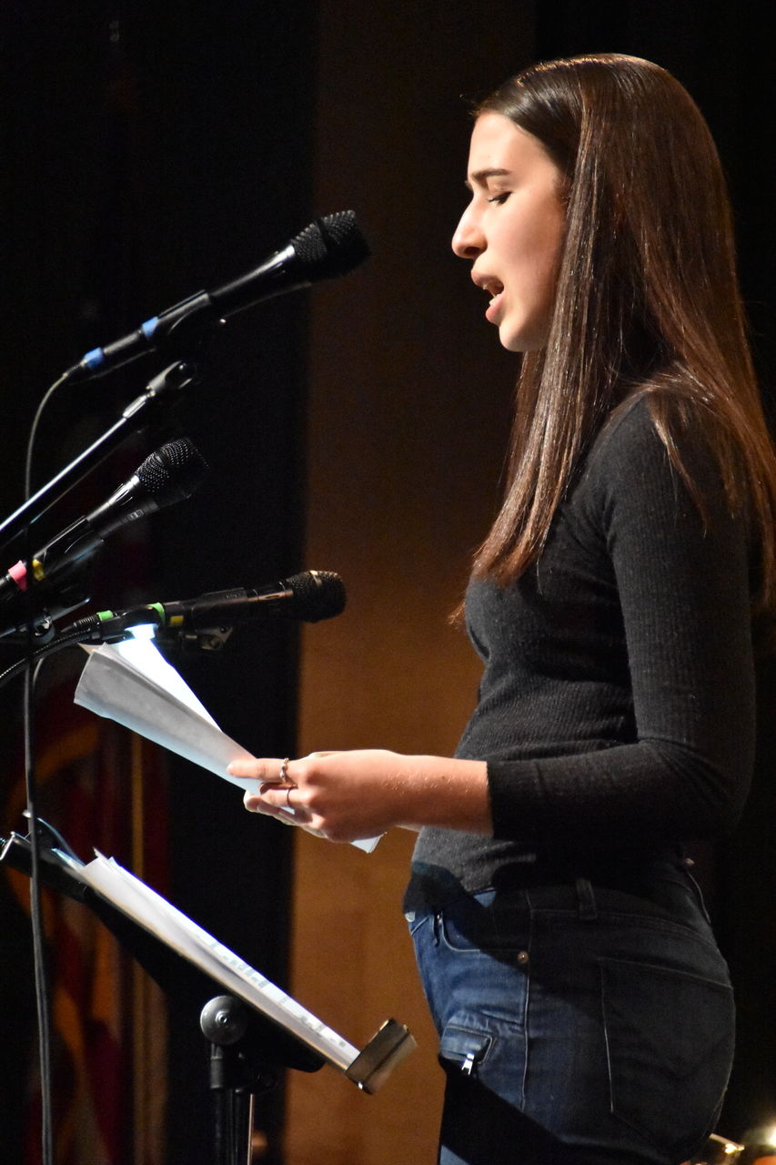 A person reading from a piece of paper on stage.