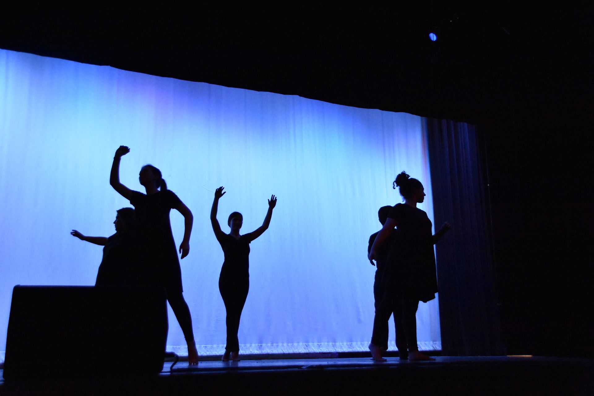 Five Dancers in silhouette in front of a baby blue background.