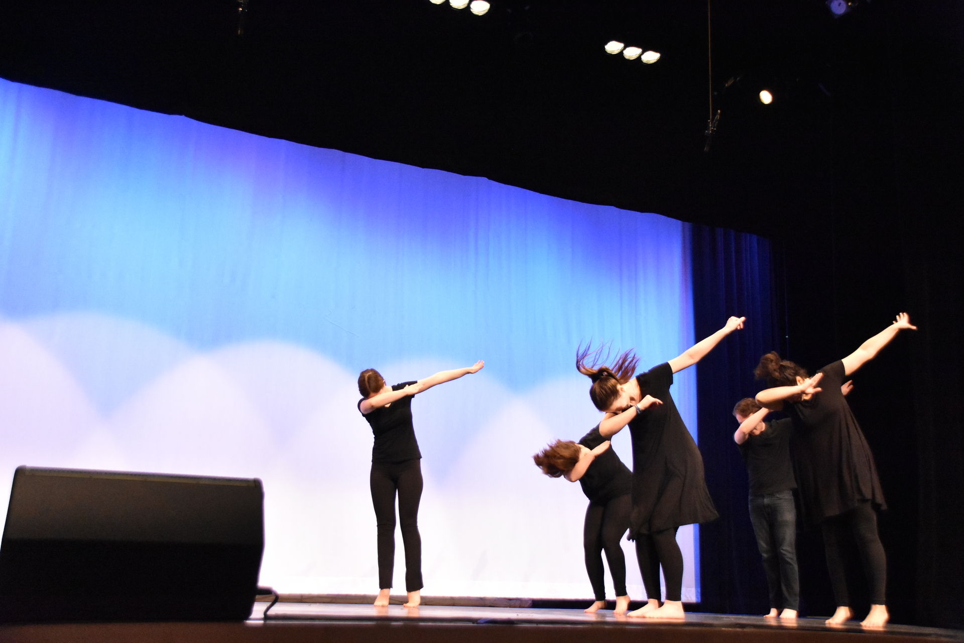Five Dancers dabbing on stage in front of a baby blue background.