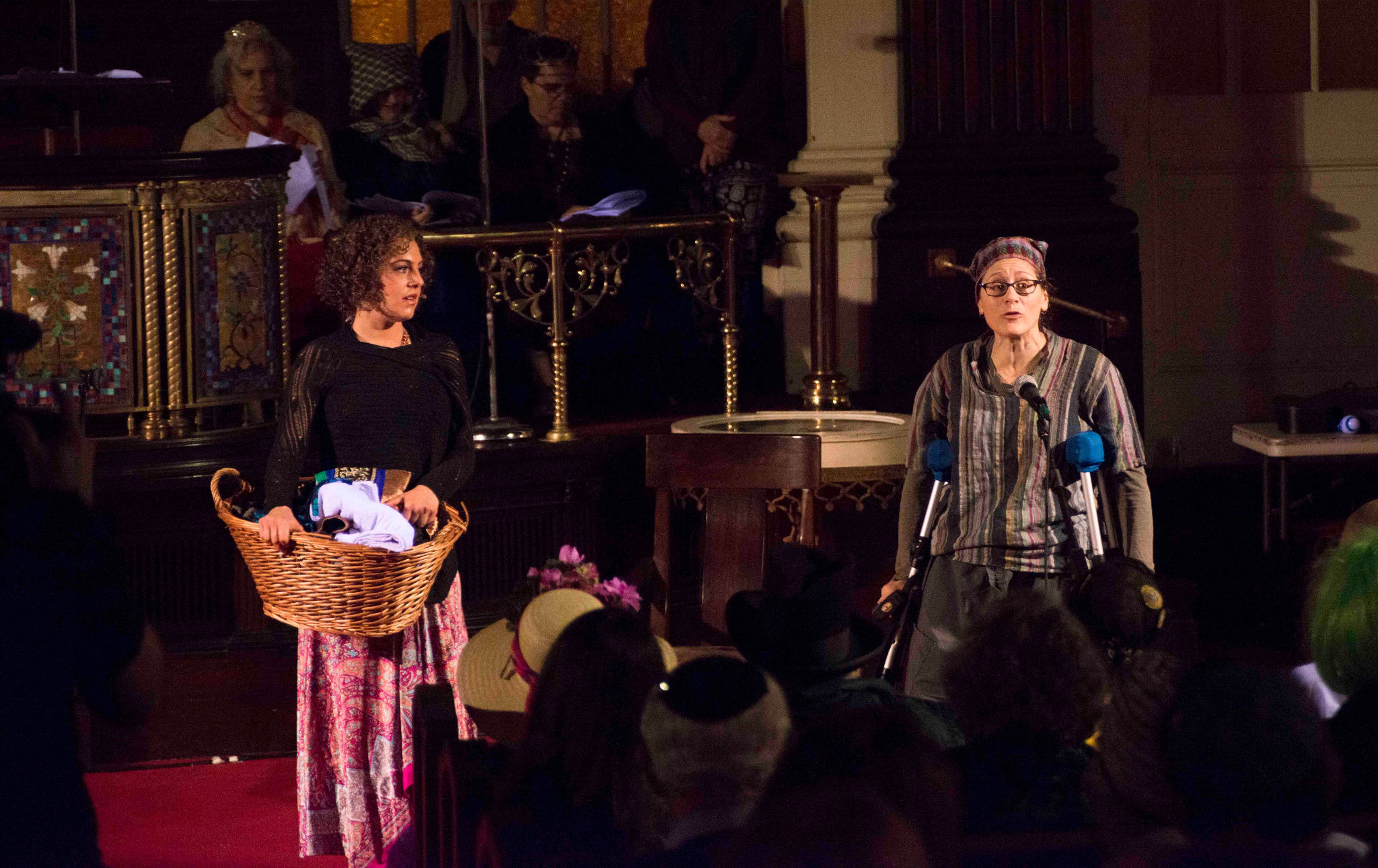A woman with a laundry basket and a woman on crutches stand on opposite sides of the stage.